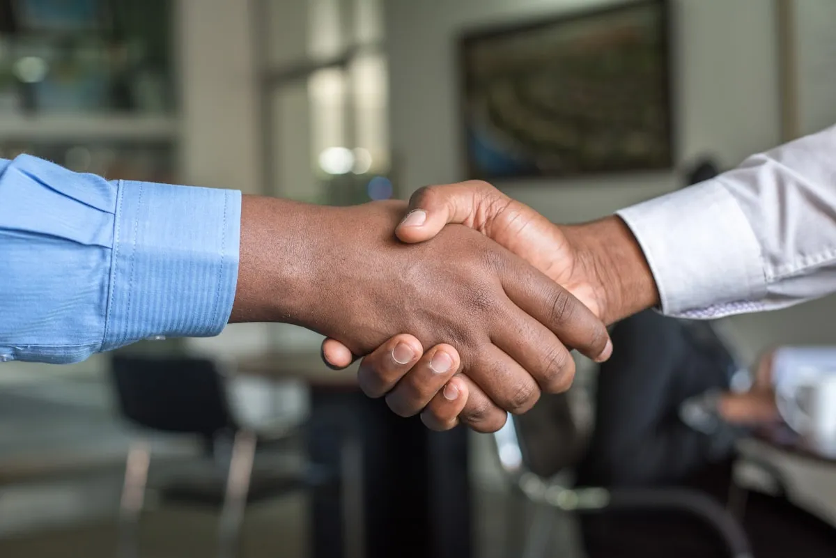 Two people shaking hands across a desk in a professional setting | Photo by Unsplash