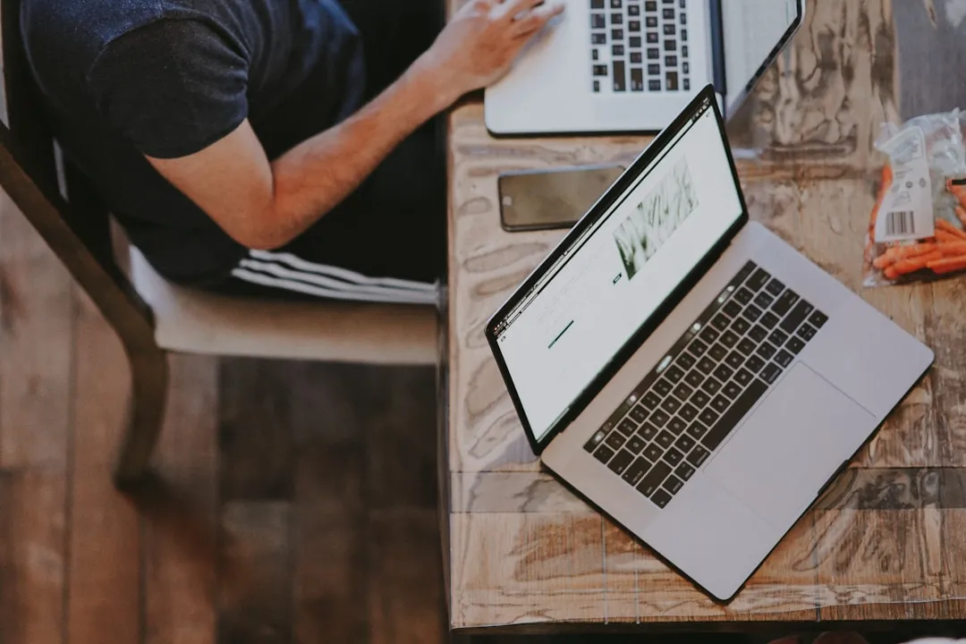 Person working from a home office with a laptop and monitor on a desk